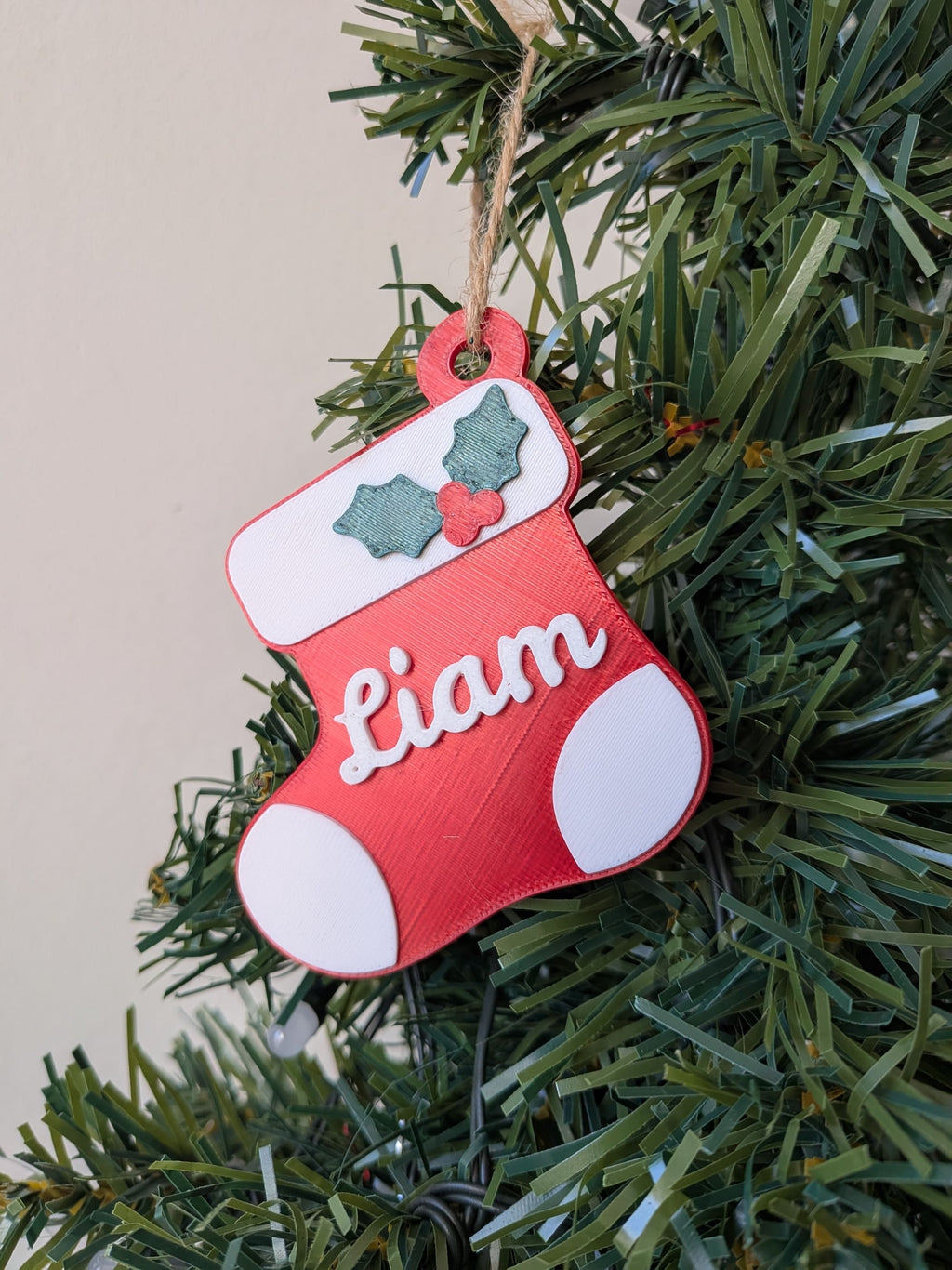 Botte de Noël rouge avec prénom Liam blanc en relief, décor de houx vert et suspension en cordelette, accrochée au sapin.