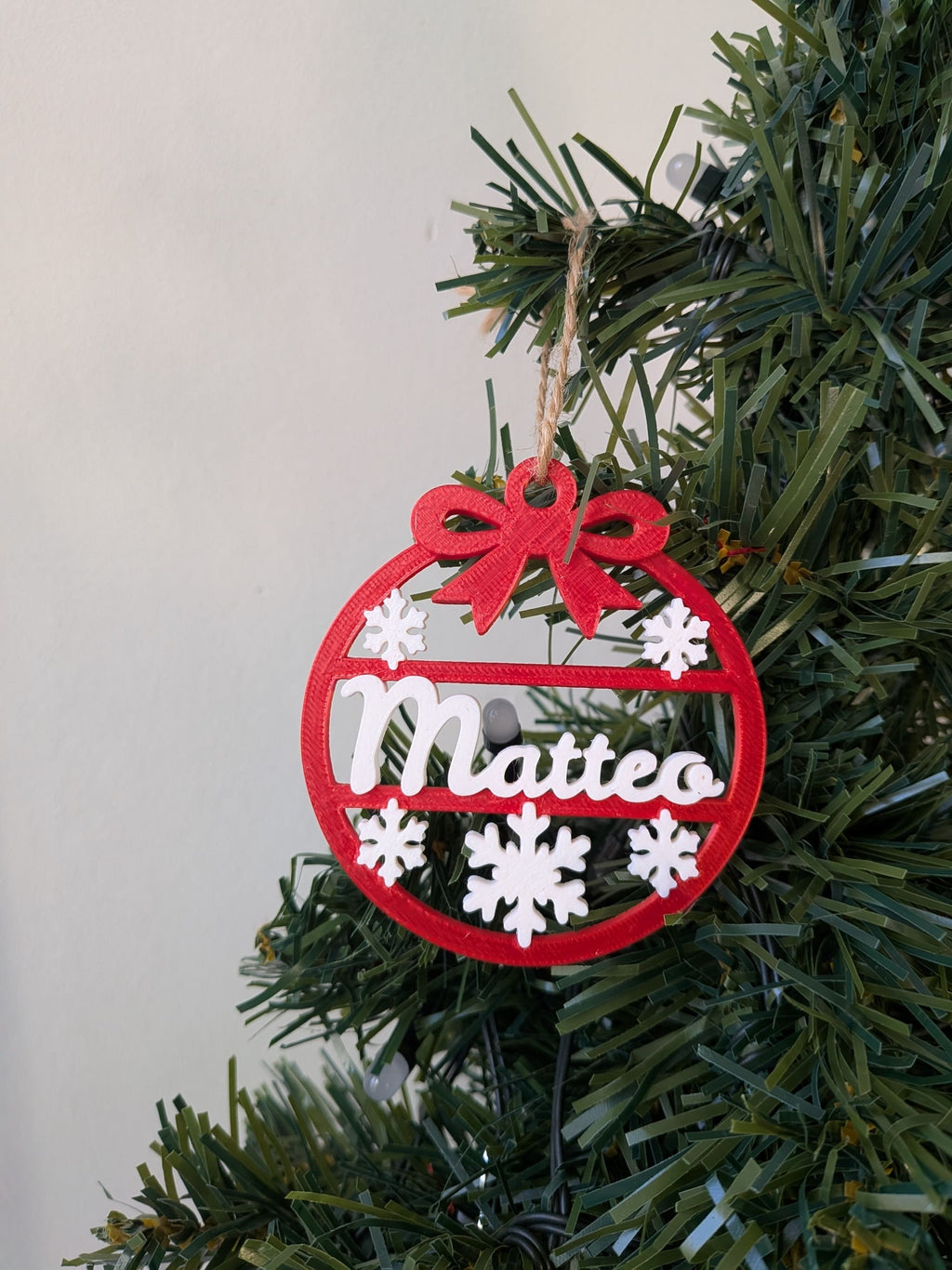 Ornement de Noël personnalisé avec prénom Matteo, boule de sapin évidée avec flocons blancs et nœud rouge.