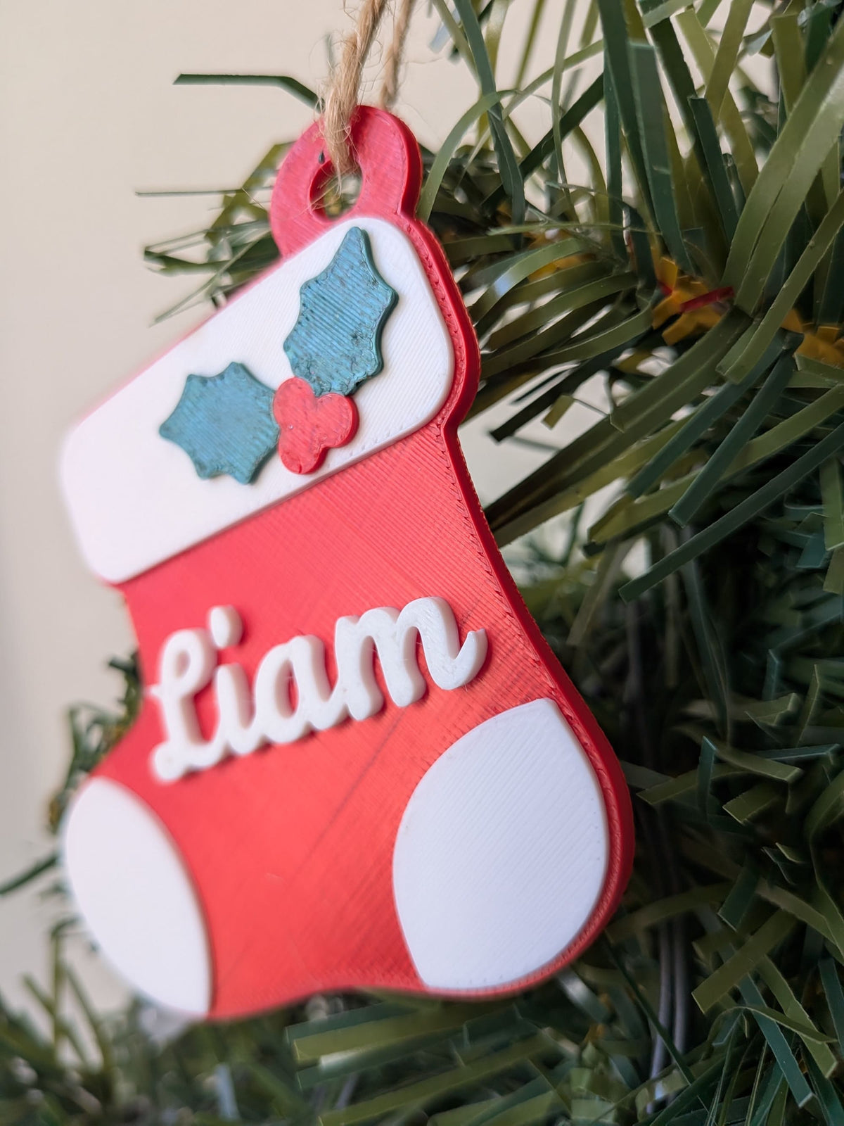 Gros plan d'une botte de Noël imprimée en 3D, montrant le prénom Liam blanc en relief et les feuilles de houx vertes.