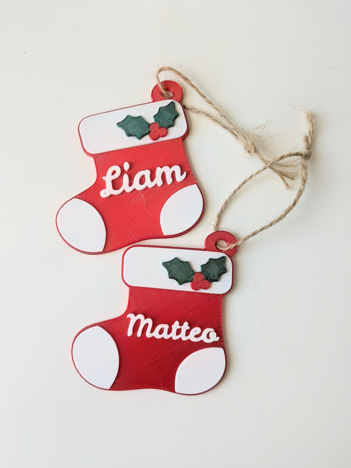 Deux bottes de Noël rouges et blanches personnalisées avec les prénoms Liam et Matteo, décorées de houx et de cordelette.
