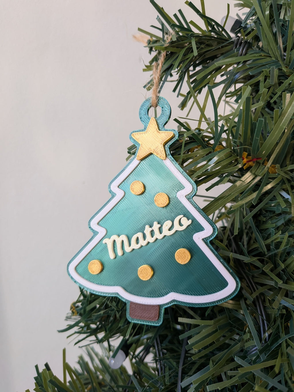 Gros plan d'un sapin de Noël vert personnalisé avec le prénom Matteo, étoile jaune, boules décoratives et bordure blanche.