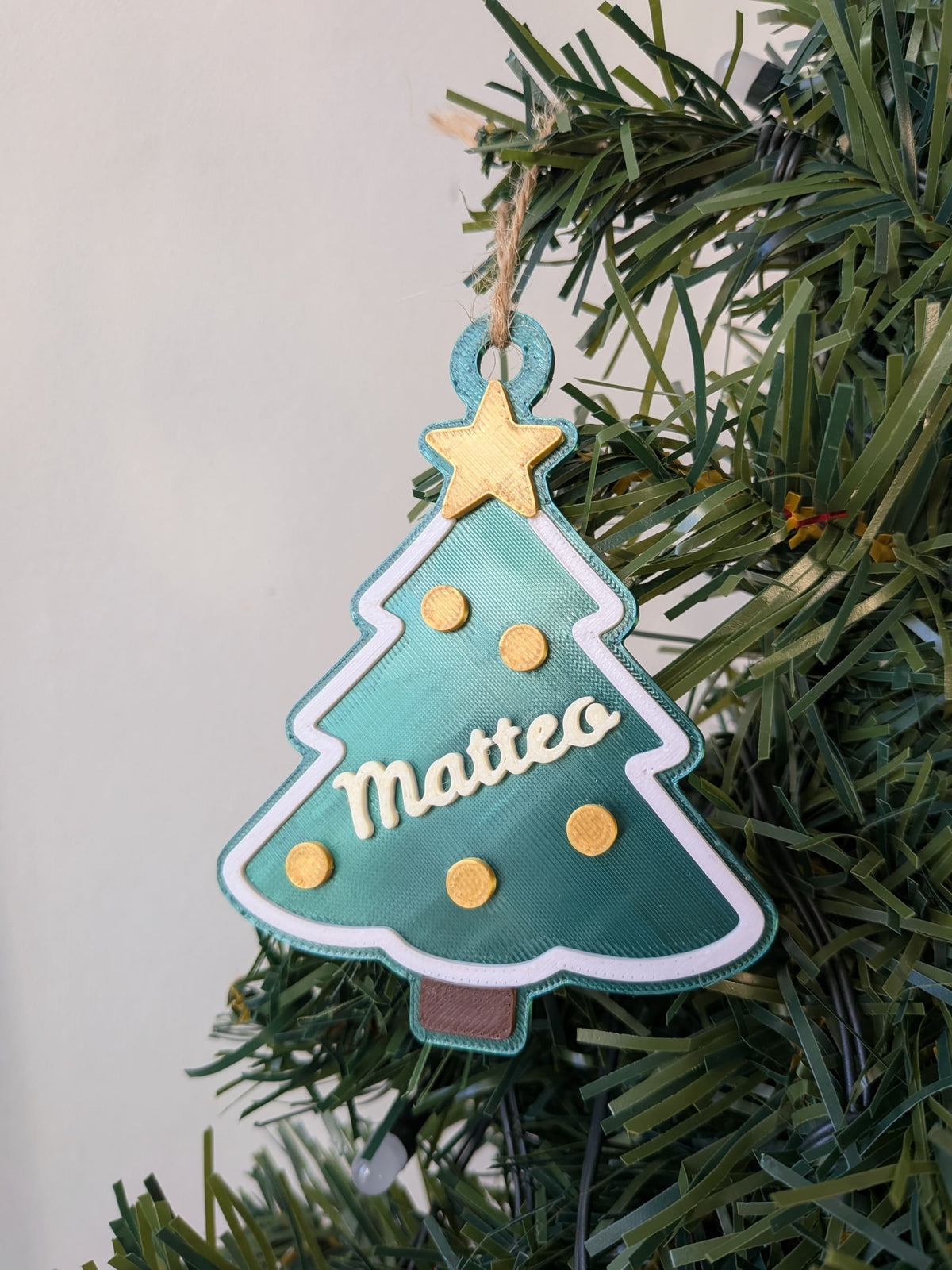 Gros plan d'un sapin de Noël vert personnalisé avec le prénom Matteo, étoile jaune, boules décoratives et bordure blanche.