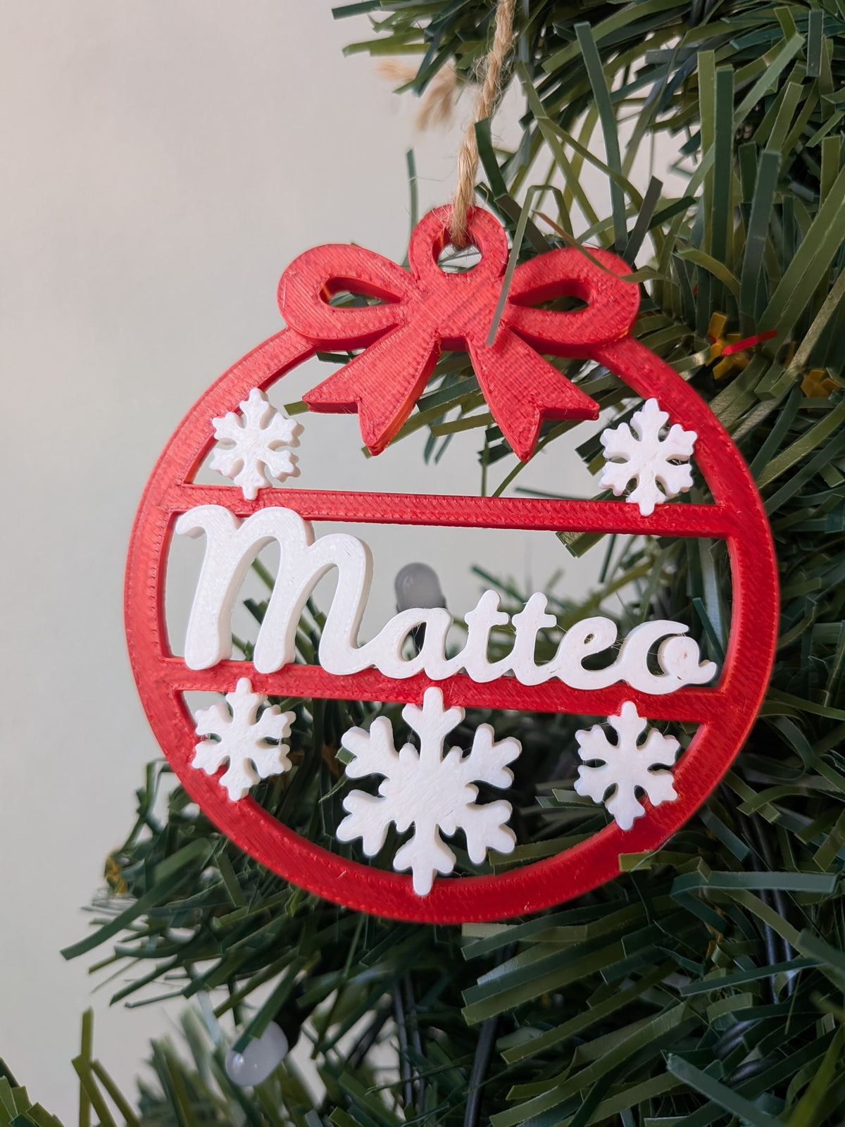 Détail d’une boule de Noël personnalisée avec prénom Matteo, décoration rouge évidée avec flocons blancs et prénom en relief.
