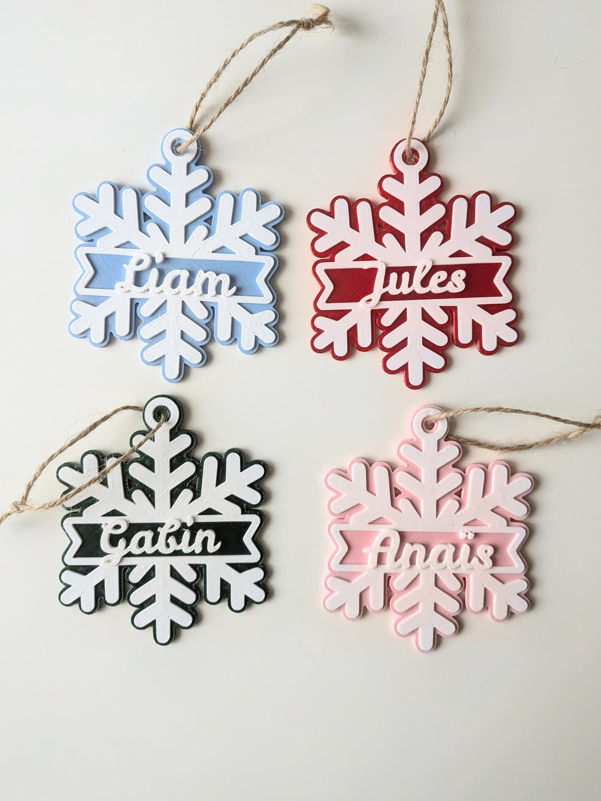 Quatre flocons de Noël personnalisés avec prénoms en relief, en bleu, rouge, vert et rose, avec cordelette de suspension.