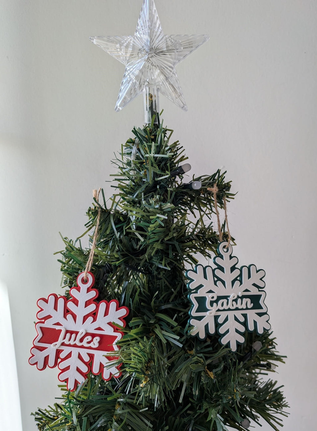 Deux flocons de Noël personnalisés avec les prénoms Jules et Gabin, rouge et vert, suspendus dans un sapin de Noël.