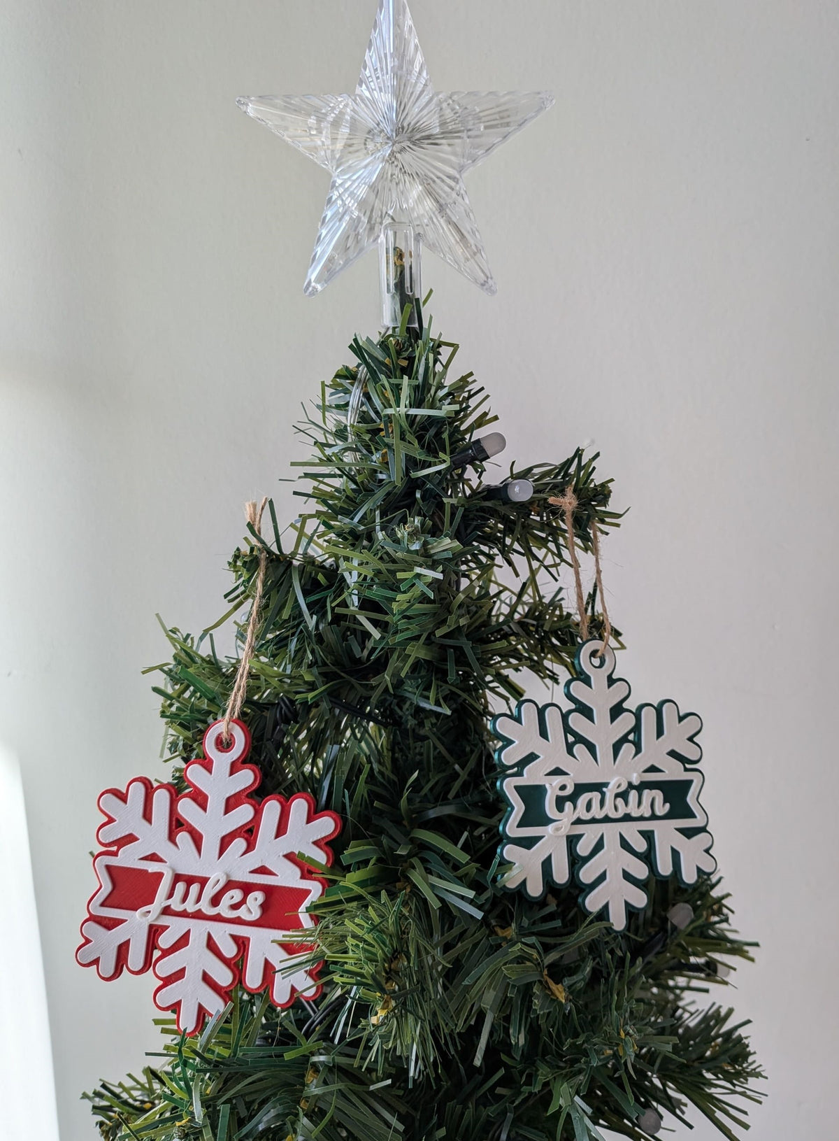 Deux flocons de Noël personnalisés avec les prénoms Jules et Gabin, rouge et vert, suspendus dans un sapin de Noël.