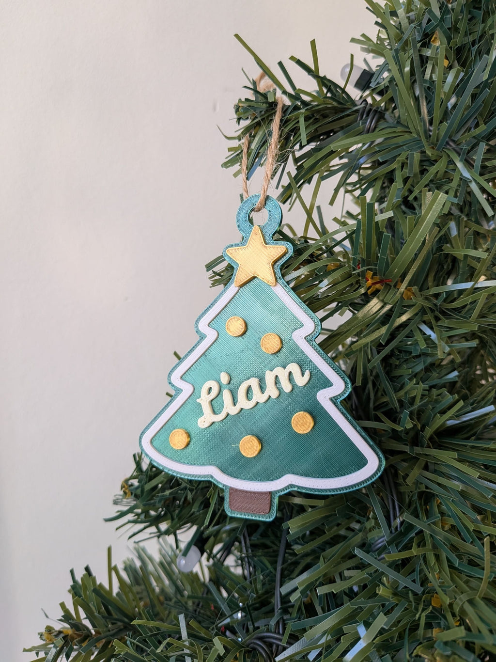 Décoration de sapin de Noël personnalisée avec le prénom Liam en relief, suspendue à une branche avec une cordelette naturelle.