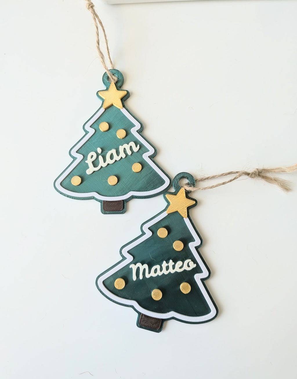 Deux ornements de Noël en forme de sapin vert, personnalisés avec les prénoms Liam et Matteo, étoile dorée et cordelette.